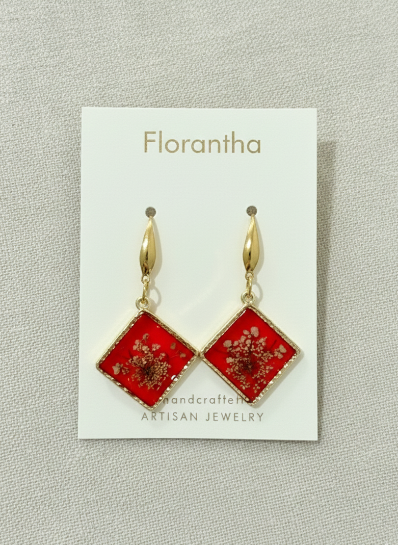 Red square earrings with gold accents on a Florantha branded card.