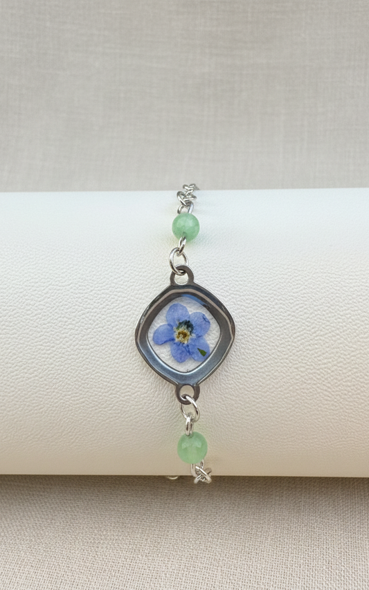 Bracelet with floral charm and green beads on a textured surface