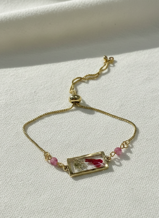 Gold bracelet with a rectangular charm and pink beads on a light background