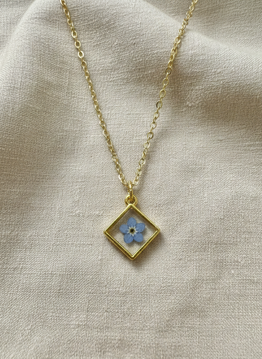 Necklace with a diamond-shaped pendant featuring a blue flower on a beige fabric background