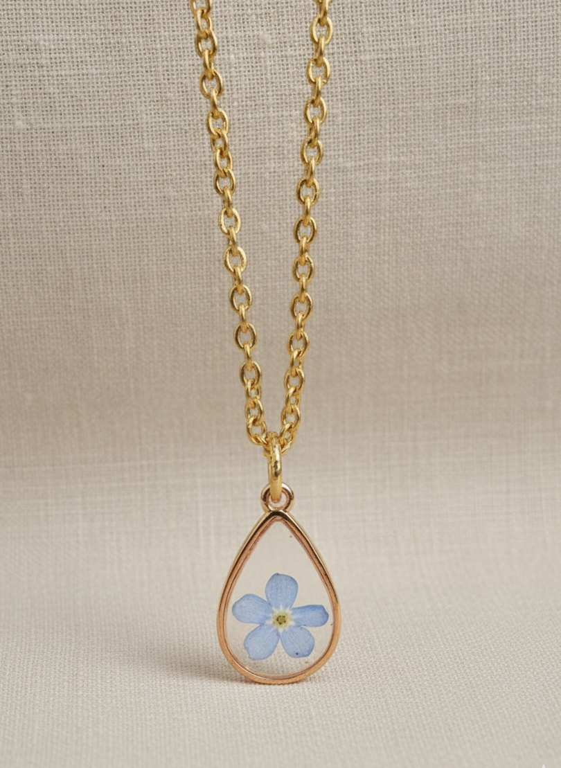 Gold necklace with a teardrop pendant featuring a pressed flower on a beige background