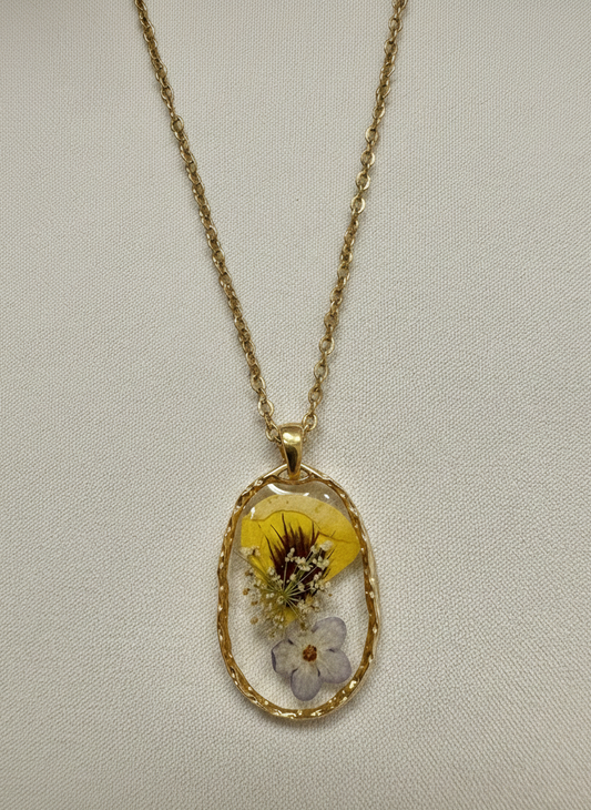 Gold necklace with a pendant featuring pressed flowers on a light gray background