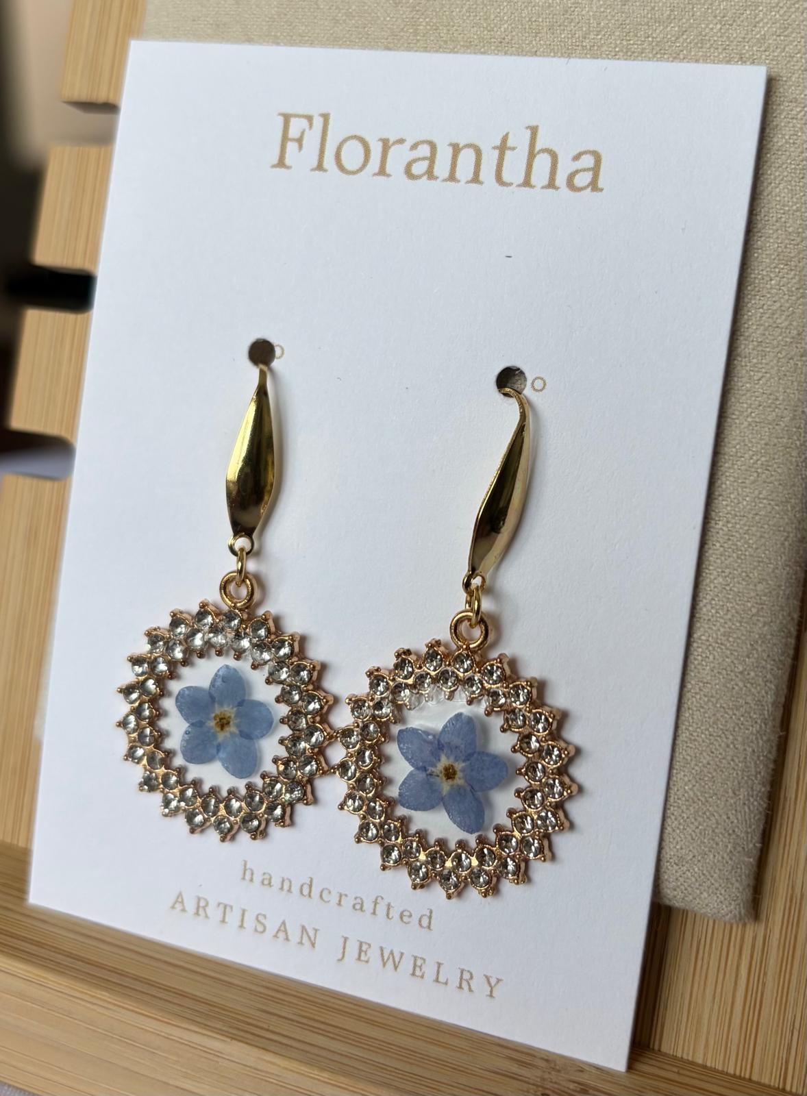 Gold earrings with floral designs on a 'Florantha' branded card.