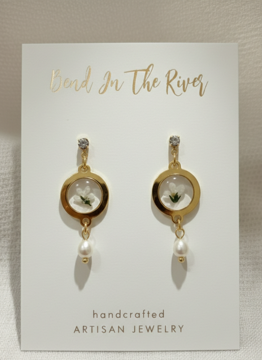 Gold earrings with floral and pearl details on a 'Bead In The River' card.